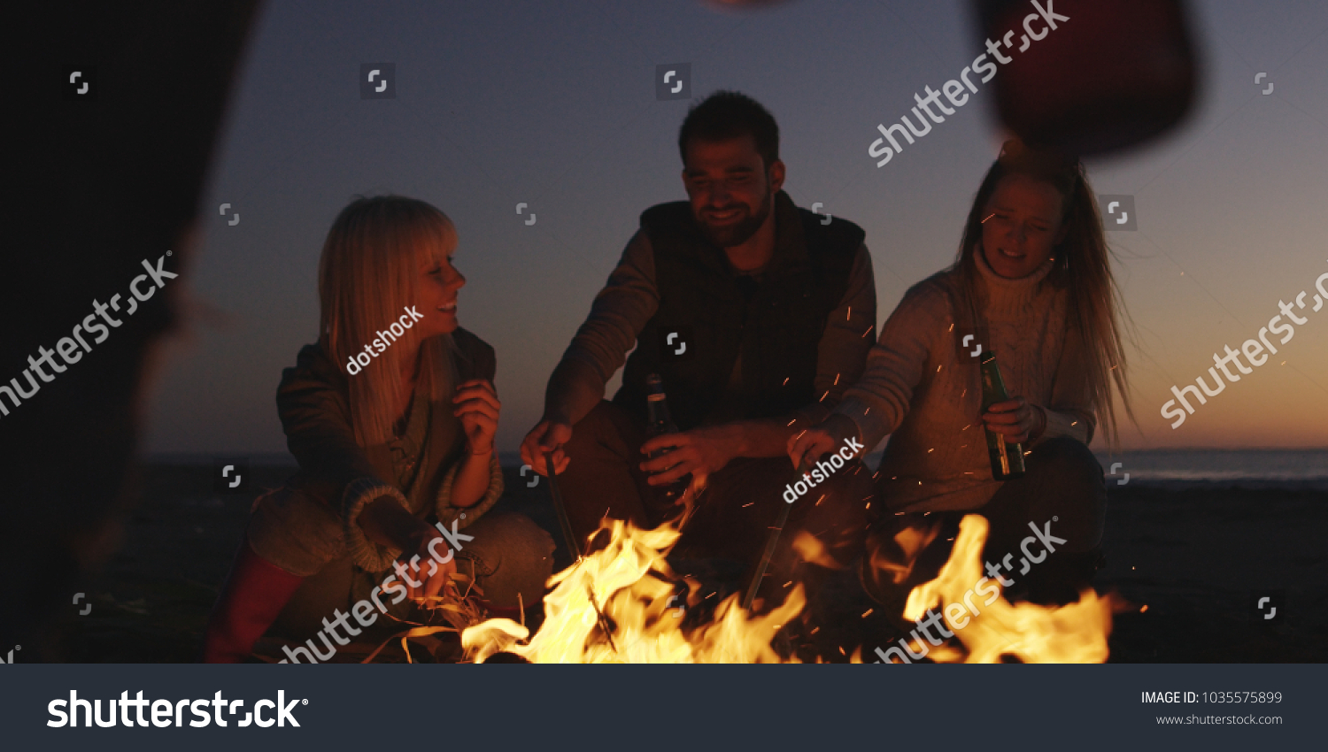 Group of young people having fun at beach around bonfire on sunset