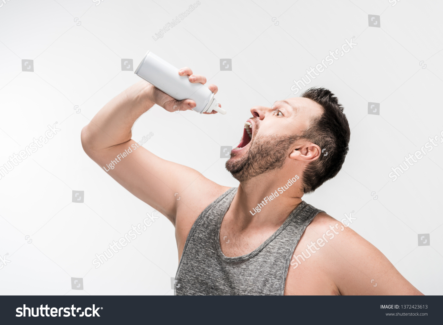 chubby man with open mouth holding bottle of whipped cream isolated on white