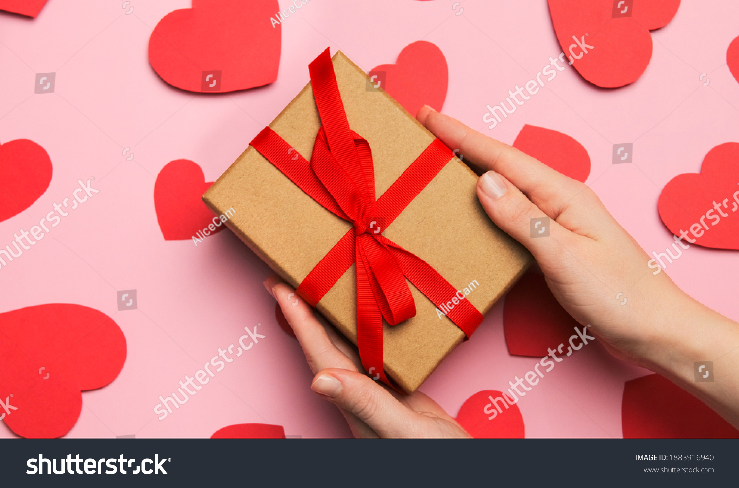 Hands hold gift box present with red bow for valentine's day declaration of love. Composition with red hearts for Valentine's Day on a pale pink background. Flat lay. Love and relationships.