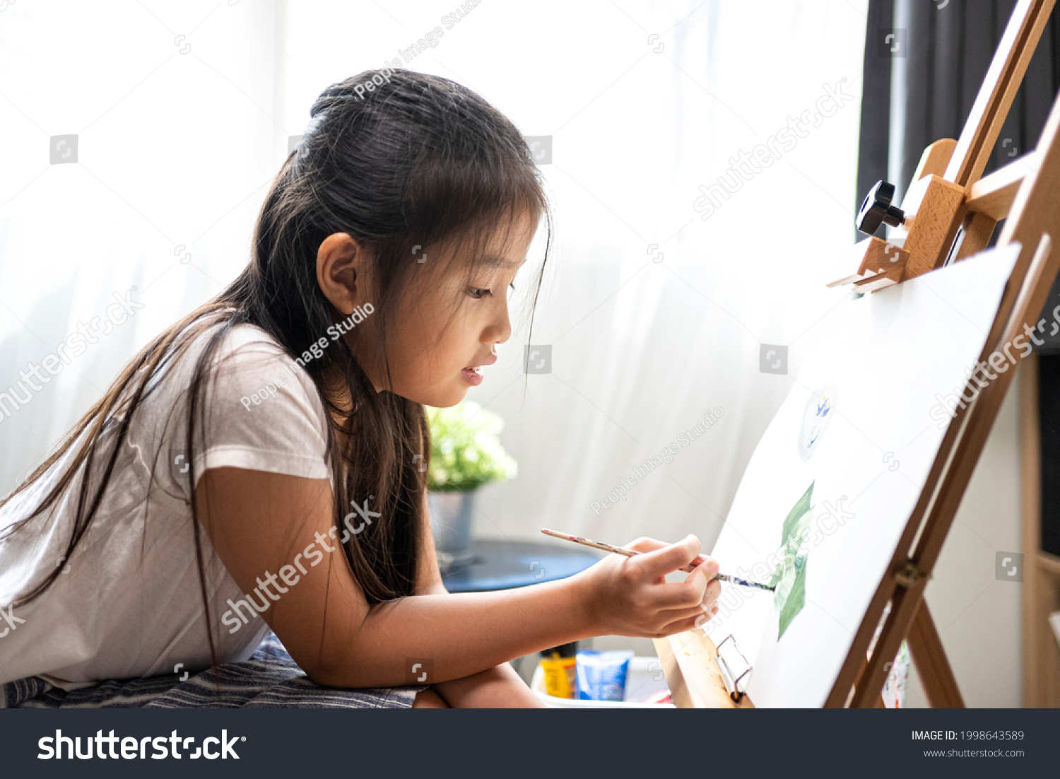 Asian beautiful girl with brush nd palette painting water color to canvas on wooden easel at home for her relaxing time.