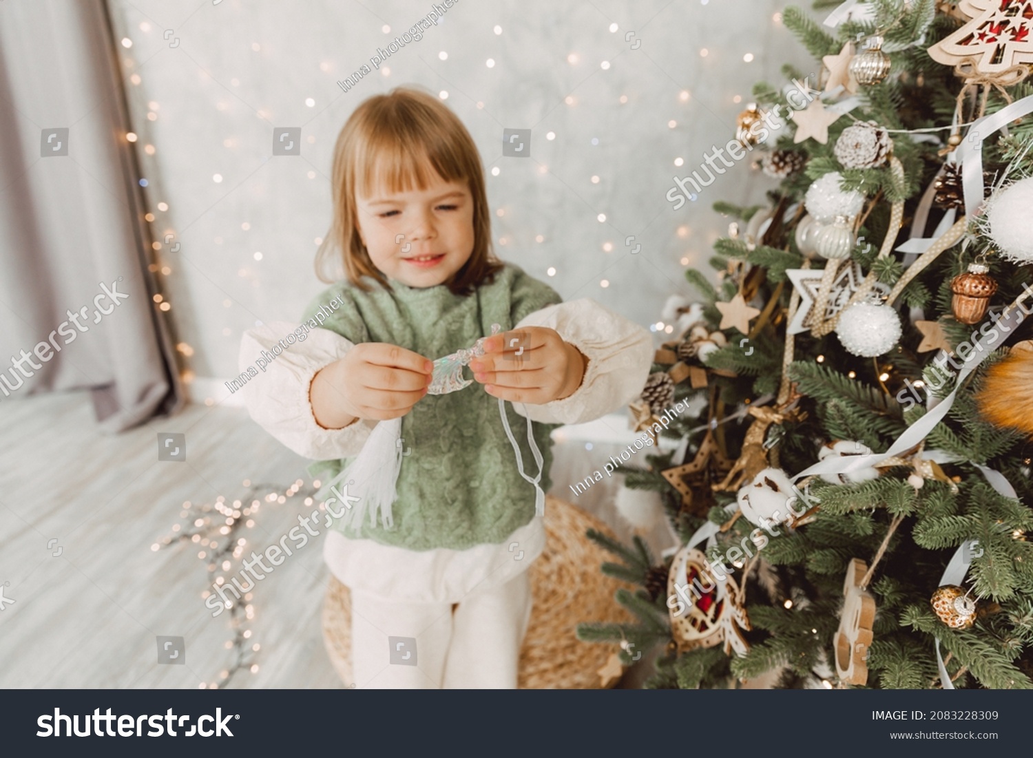 Little girl decorates the Christmas tree with toys. A cute baby is preparing at home for the celebration of Christmas.