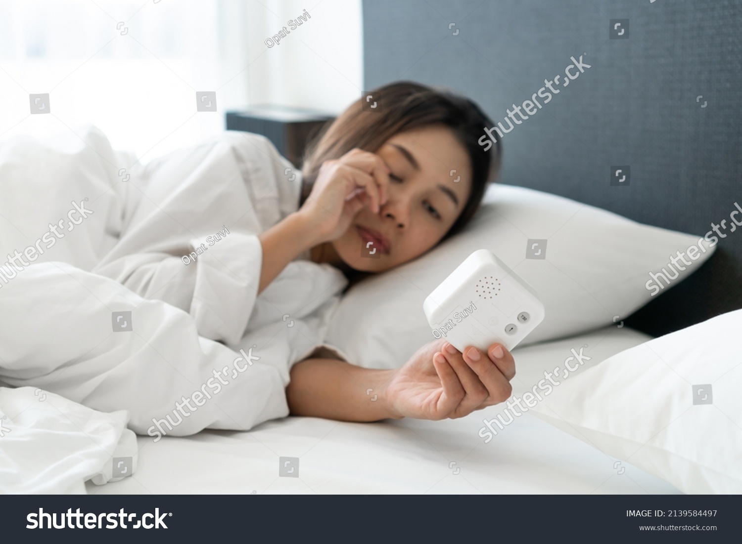 Sleepy young Asian woman lying in bed turning off an alarm clock in the morning