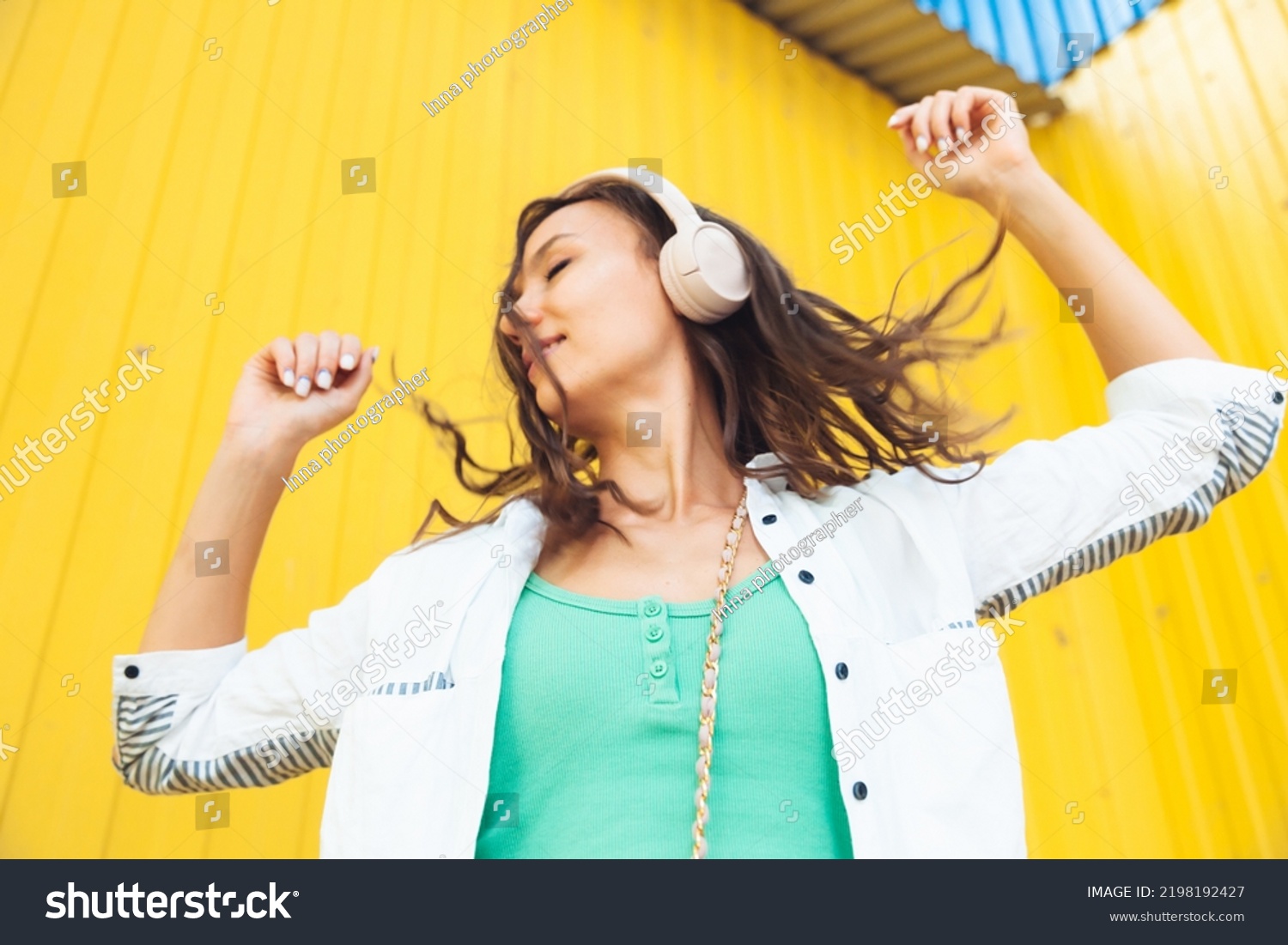 A full-length view of a beautiful cheerful girl jumping while listening to a melody isolated against a bright yellow background. a young woman with headphones dancing on the street . generation z