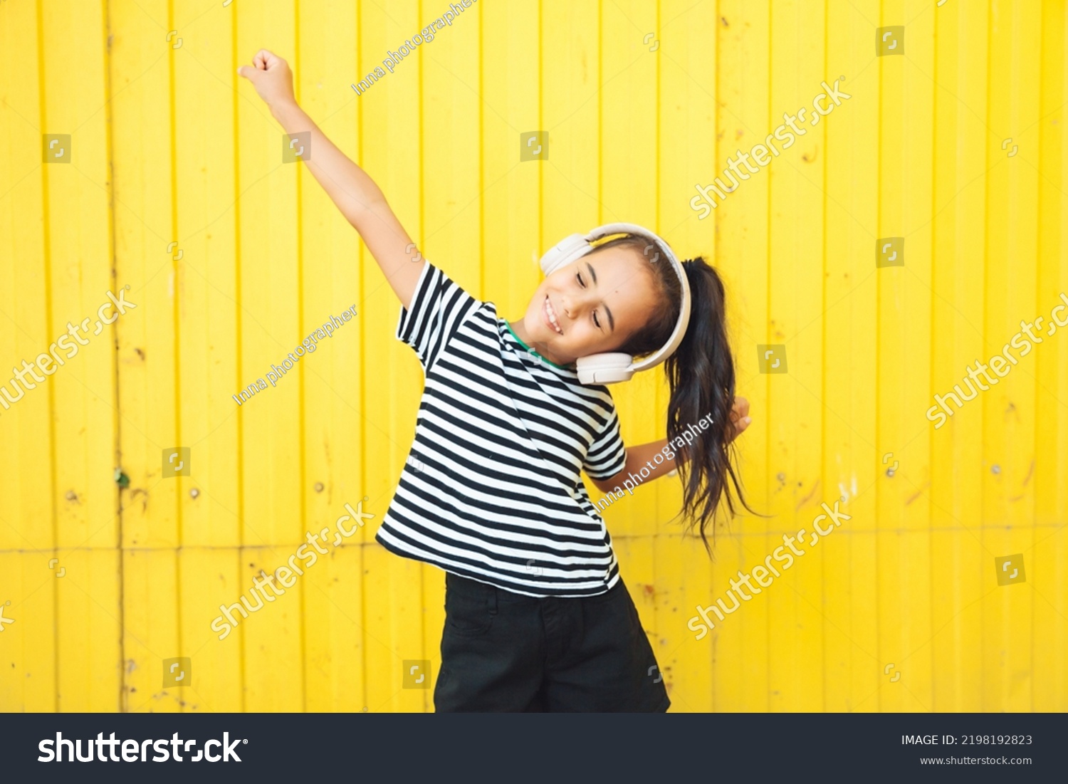 A child with headphones listening to music. Audiobook concept. Learning audio lessons. a little girl with headphones listening to music. a child is dancing on the background of a yellow fence