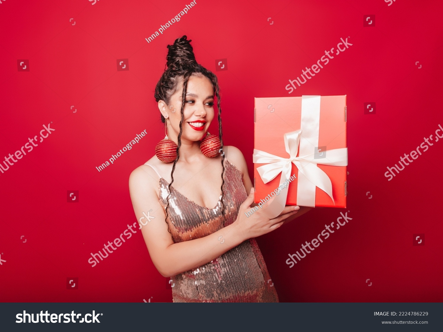 A woman in a red Christmas hat with dreadlocks holds a gift on a red background. Isolate. a woman in a smart dress. new year christmas