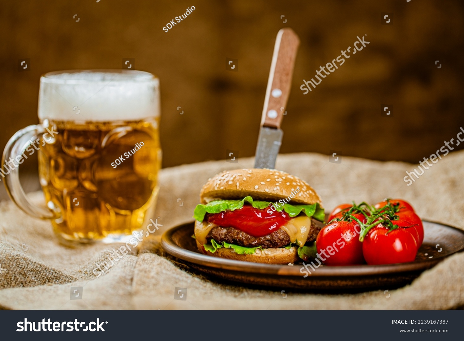 Front view of fresh homemade beef burger with knife on rustic wooden serving table with glass of beer. Selective focus. 