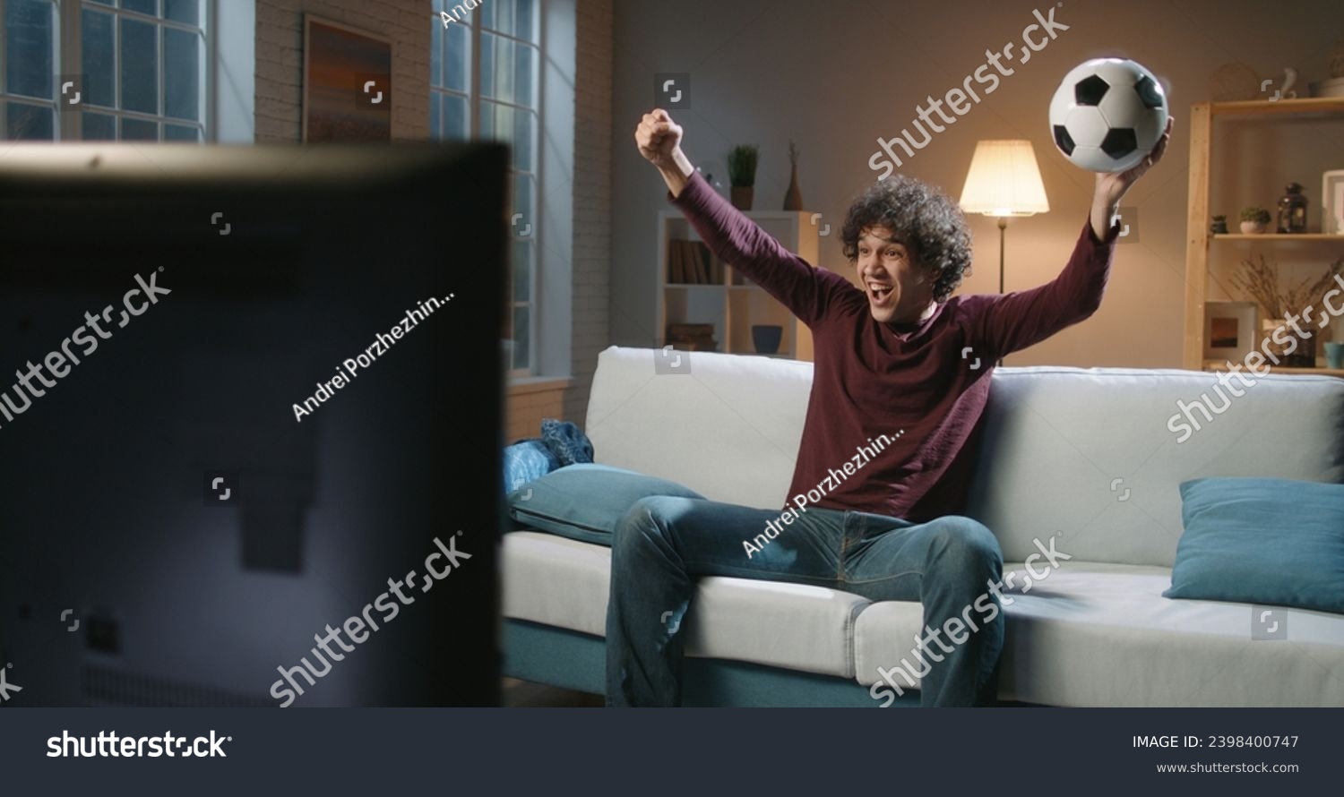 At Home Joyful Sports Fan With the Ball in Hands Sitting on a Couch Watch Game on TV Cheer Shout. Celebrate Victory when Sports Team Wins Championship.