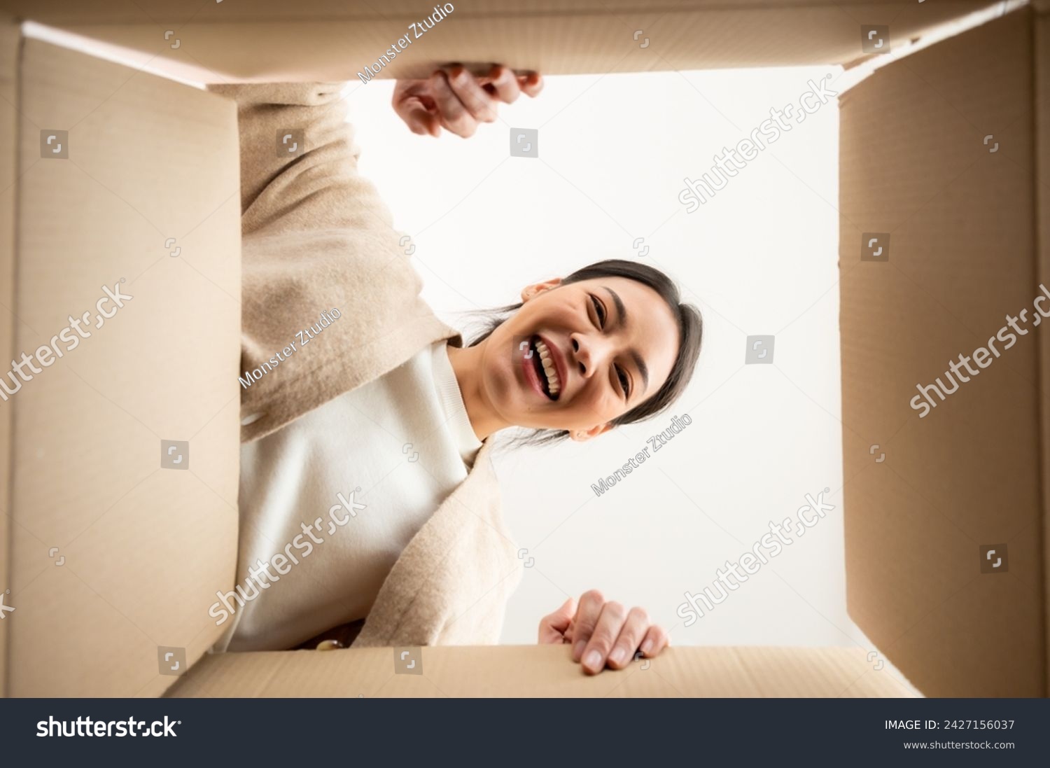 Surprised young asian woman unpacking. Opening carton box and looking inside. Packaging box delivery service. Human emotions and facial expression