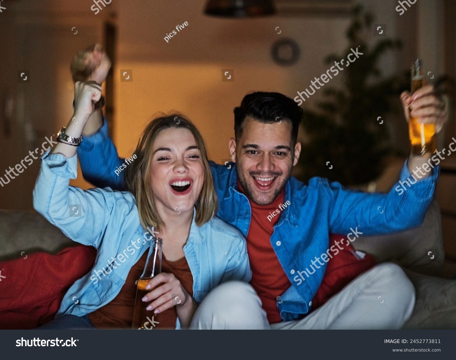 Portrait of an excited young couple watching tv and screaming while drinking beer and cheering for their national soccer team victory