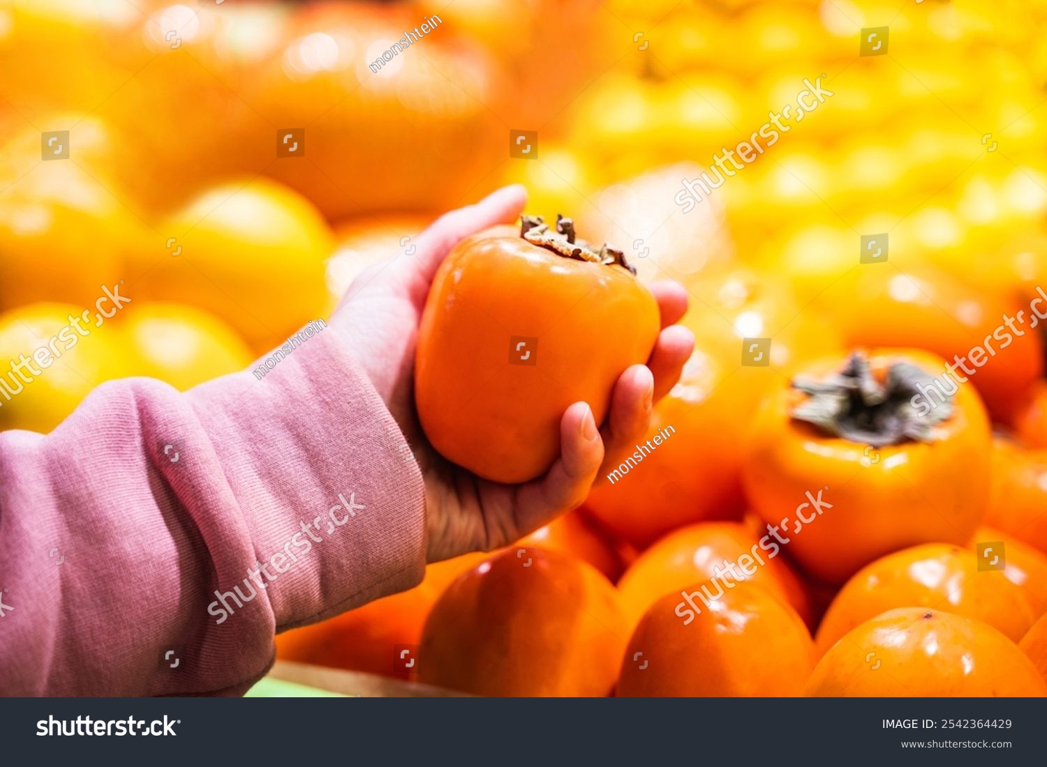 Woman holding fresh persimmon near fruit counter at market closeup of female hand picking fresh persimmon at supermarket grocery shopping concept