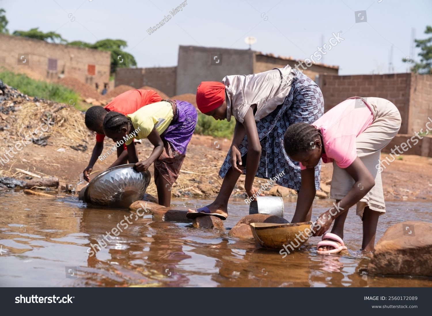 Group of West African village girls washing dishes in the stagnant water of a dirty river