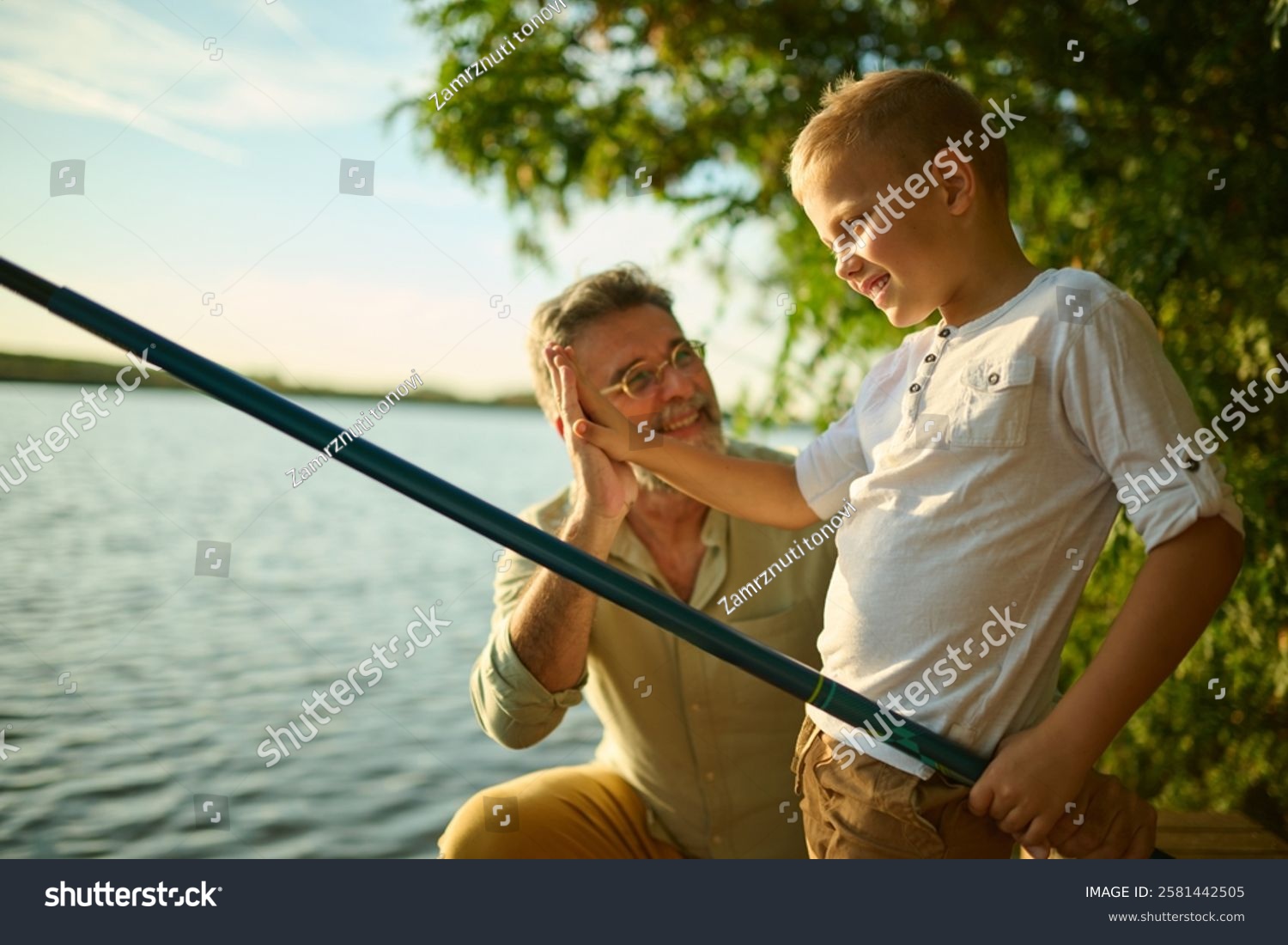 Grandfather and grandson fishing by a tranquil lake enjoying nature and creating memories. High fiving in golden sunlight cherishing togetherness