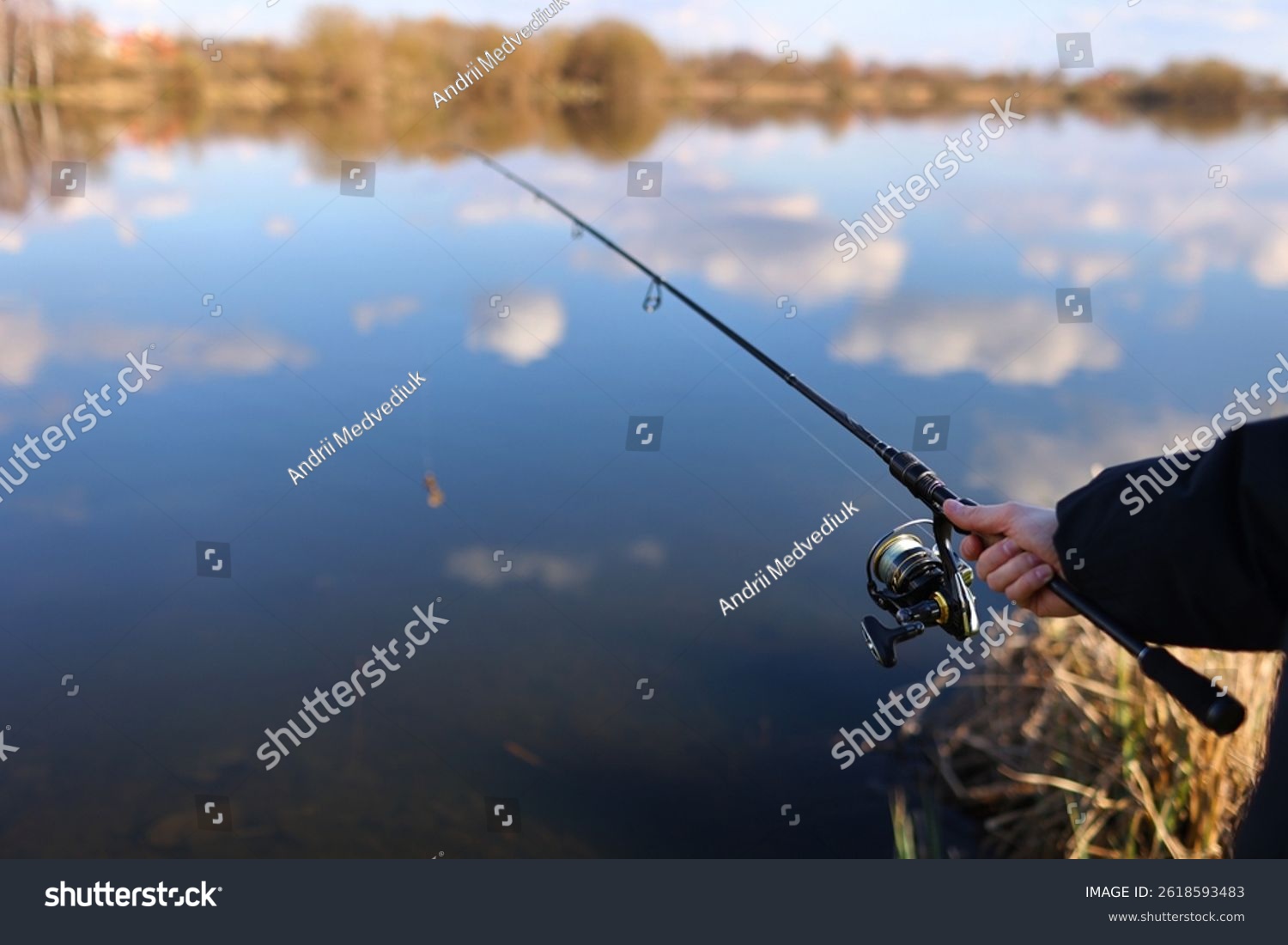 Man catching fish pulling rod while fishing from lake or pond. Fisherman with rod spinning reel on river bank. Fishing for pike perch carp on beach lake or pond. Wild nature rural getaway