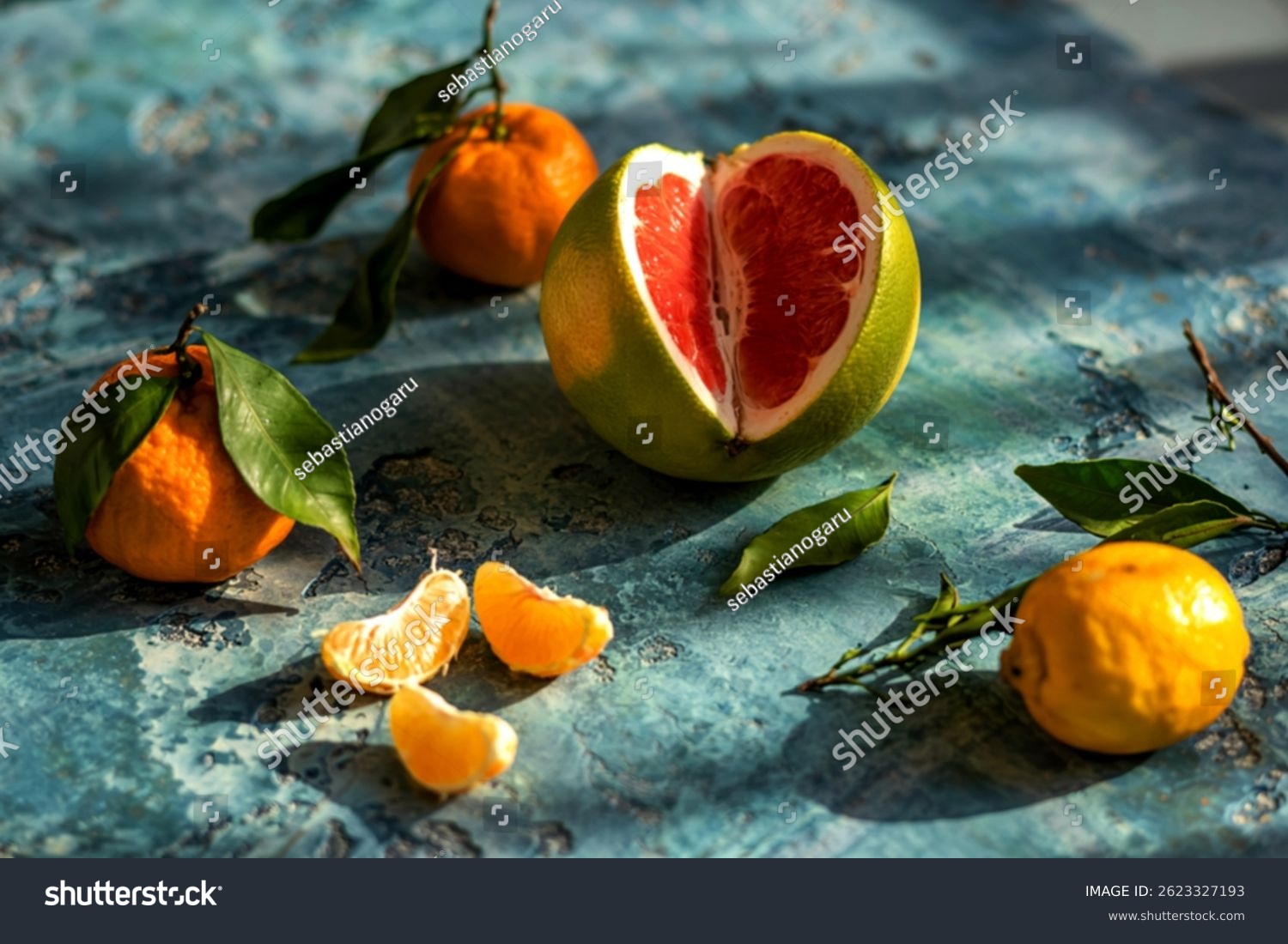 Pomelo red inside with tangerine and lemons lies on blue concrete