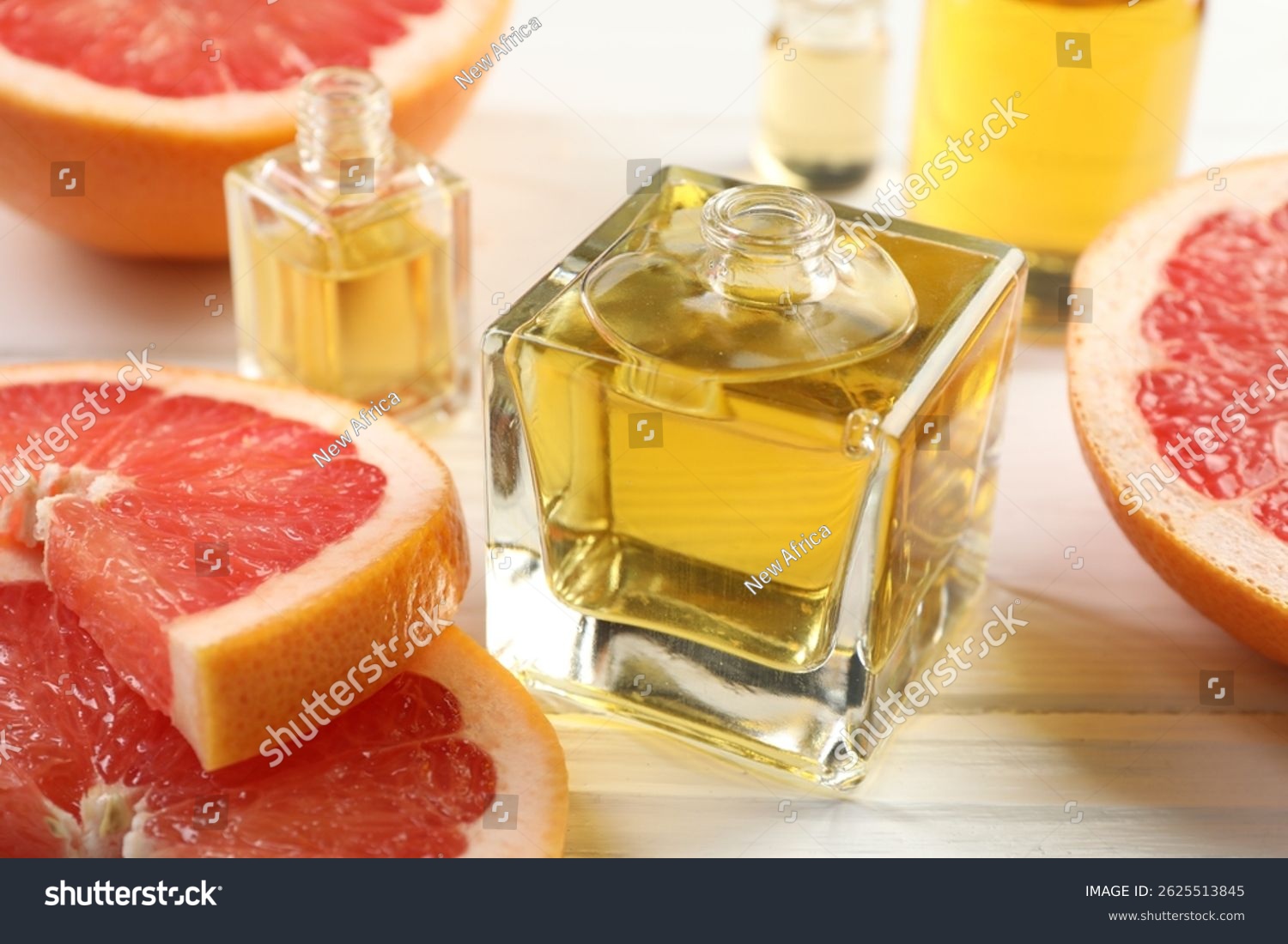 Open perfume bottles with aromatic essential oils and slices of grapefruit on white wooden table closeup