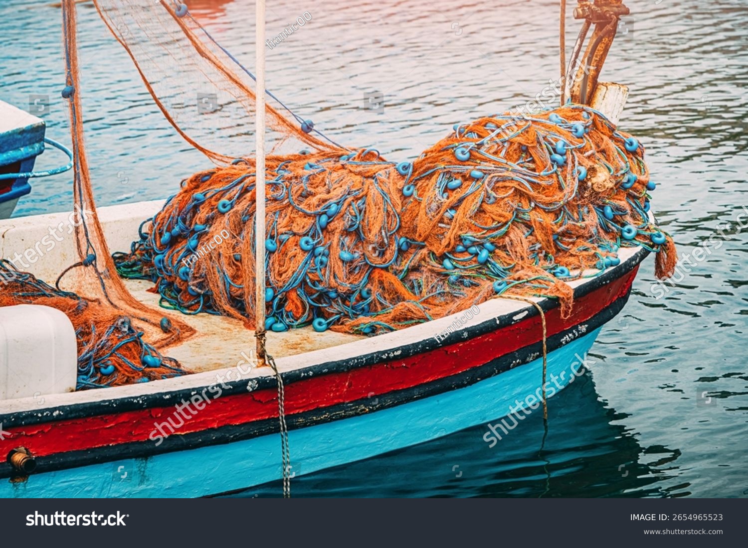 fishing nets with blue floats are lying on the bow of a small colorful fishing boat gently floating on the calm water of a harbor