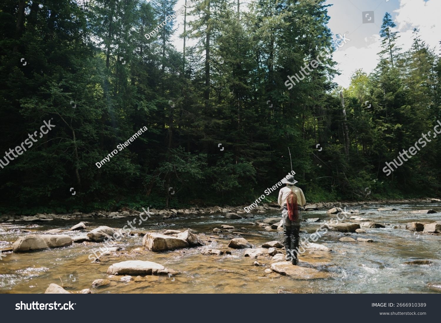 Fisherman casts his line into a clear river flowing through a tranquil forest enjoying the serenity of nature while fly fishing